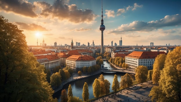 Blick auf den Berliner Fernsehturm bei Sonnenuntergang, umgeben von historischer Architektur und grünen Baumalleen.