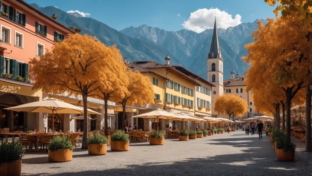Gemütliche Straße in Meran mit orangefarbenen Bäumen, Cafés, Bergen im Hintergrund und blauen Himmel.