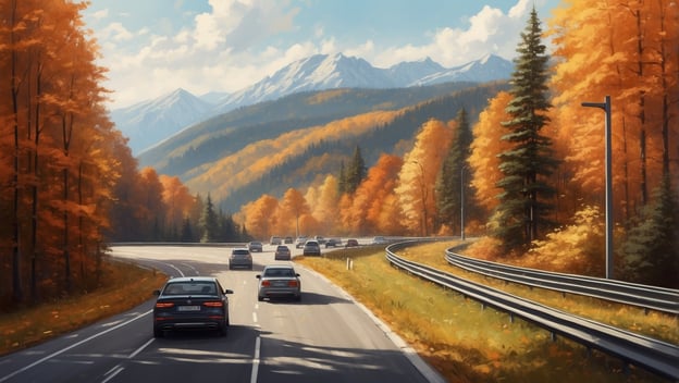 Blick auf eine Herbststraße mit mehreren Autos, umgeben von buntem Laub und Bergen im Hintergrund.