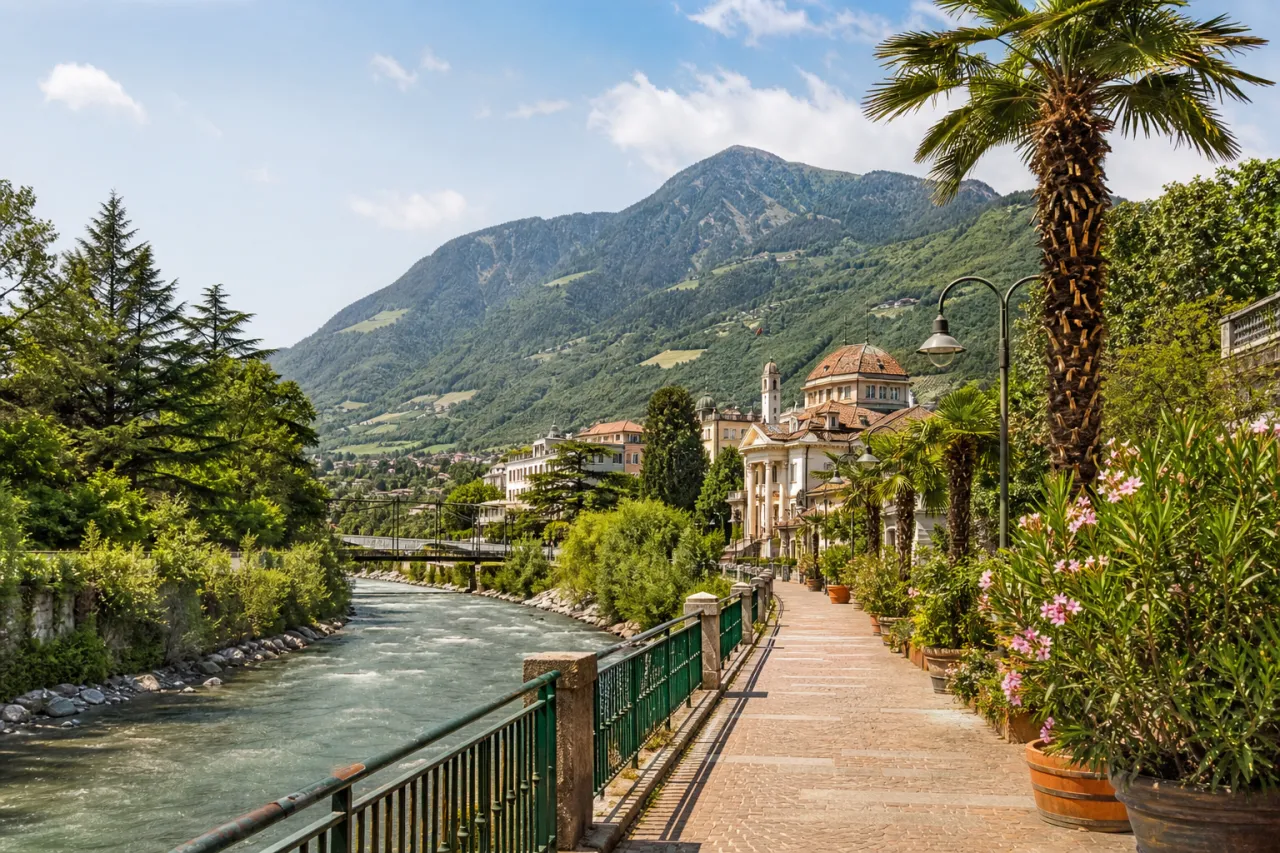 Passerpromenade Meran mit blühenden Palmen und Blick auf die Südtiroler Bergkulisse im Sommer